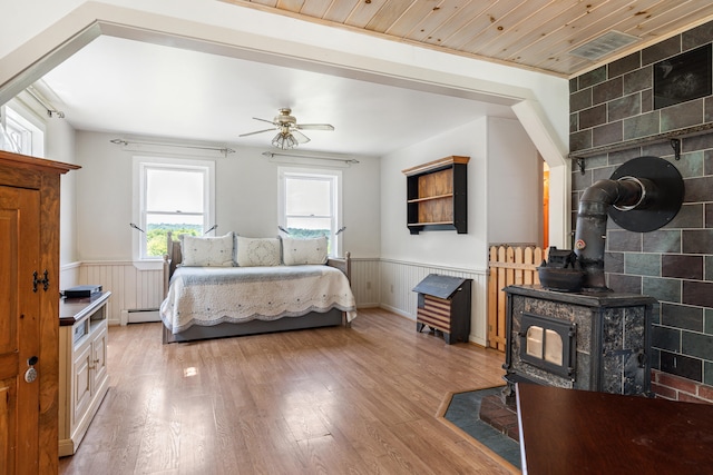 bedroom featuring ceiling fan, light hardwood / wood-style floors, a wood stove, and wooden ceiling