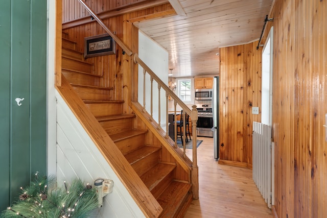 stairway featuring light hardwood / wood-style floors, wood walls, and wooden ceiling