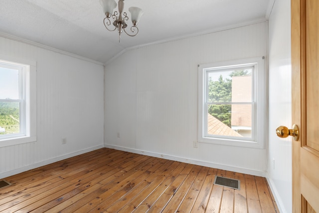 unfurnished room with a healthy amount of sunlight, a notable chandelier, hardwood / wood-style floors, and vaulted ceiling