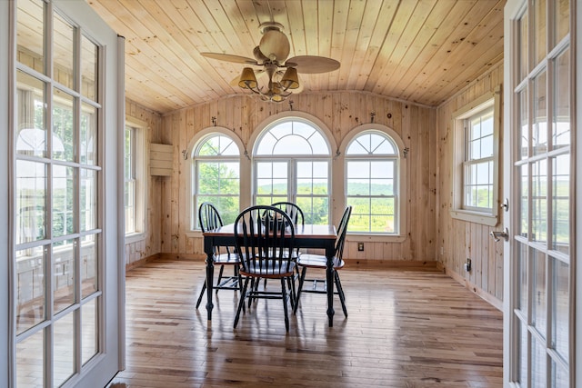 dining room featuring light hardwood / wood-style flooring, wood walls, and lofted ceiling