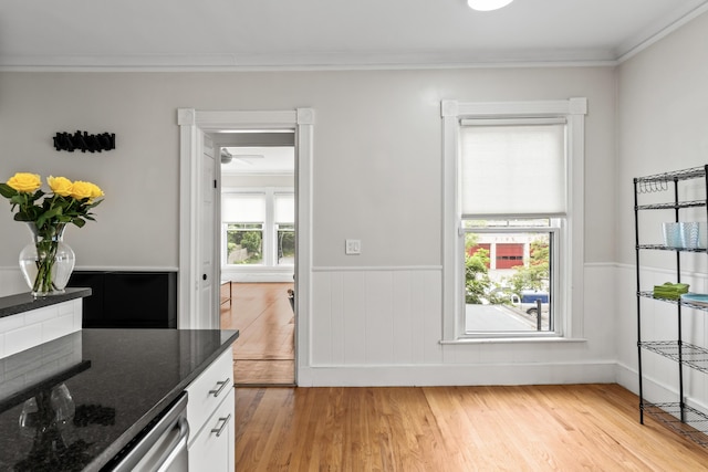 kitchen with crown molding, stainless steel dishwasher, dark stone countertops, light hardwood / wood-style floors, and white cabinetry