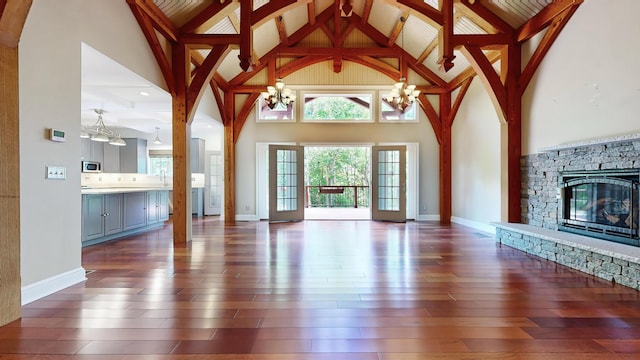 unfurnished living room with beam ceiling, dark wood-type flooring, a stone fireplace, high vaulted ceiling, and a chandelier