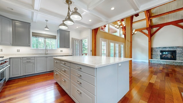 kitchen featuring a stone fireplace, gray cabinetry, decorative light fixtures, a kitchen island, and sink