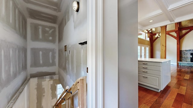 bathroom with coffered ceiling, hardwood / wood-style flooring, a stone fireplace, a chandelier, and beamed ceiling