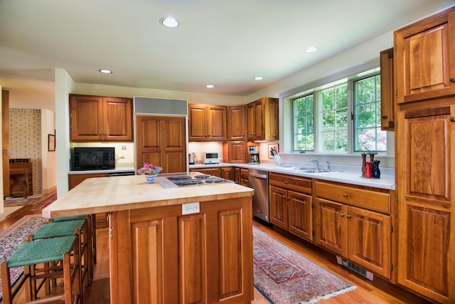 kitchen featuring appliances with stainless steel finishes, a center island, a kitchen bar, a brick fireplace, and light hardwood / wood-style flooring