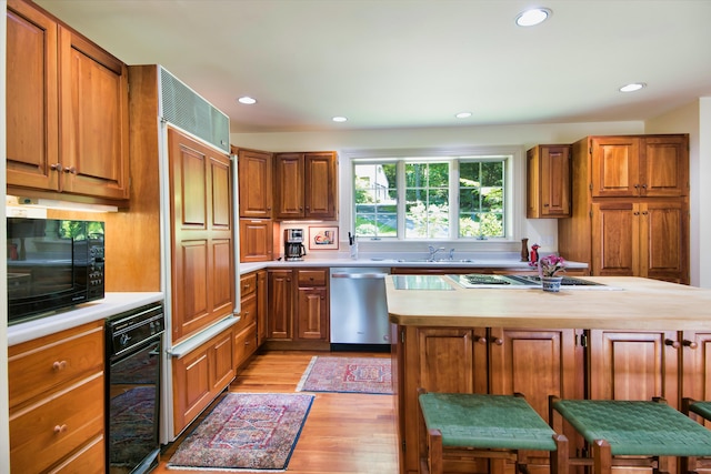 kitchen with a center island, black microwave, a kitchen breakfast bar, light wood-type flooring, and stainless steel dishwasher