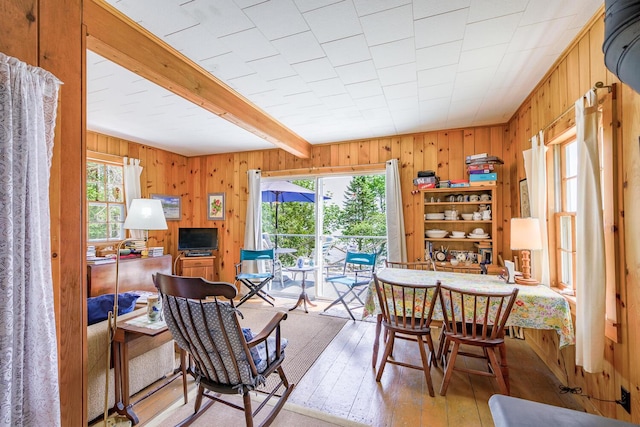 dining room featuring beam ceiling, light hardwood / wood-style flooring, wooden walls, and a healthy amount of sunlight