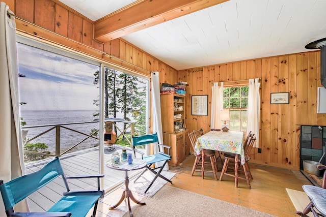 dining room featuring light hardwood / wood-style flooring, beamed ceiling, and wood walls