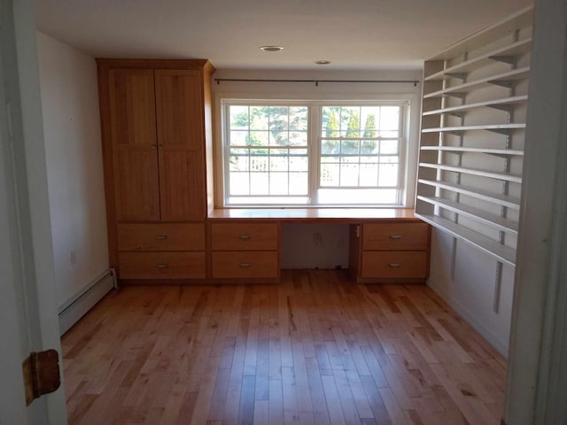 interior space with built in desk, a baseboard heating unit, and light hardwood / wood-style flooring