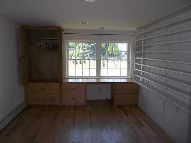 unfurnished room with built in desk, light hardwood / wood-style flooring, and a baseboard radiator