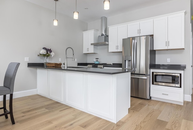 kitchen featuring white cabinets, hanging light fixtures, kitchen peninsula, stainless steel appliances, and wall chimney range hood