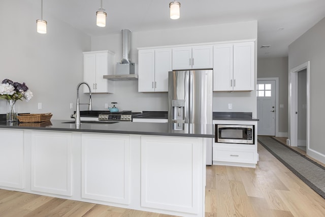 kitchen with pendant lighting, wall chimney range hood, sink, appliances with stainless steel finishes, and white cabinetry