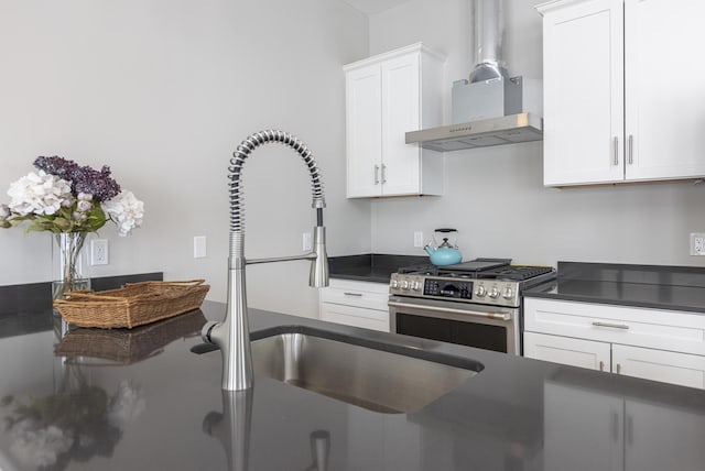 kitchen with white cabinets, stainless steel gas range, sink, and wall chimney range hood