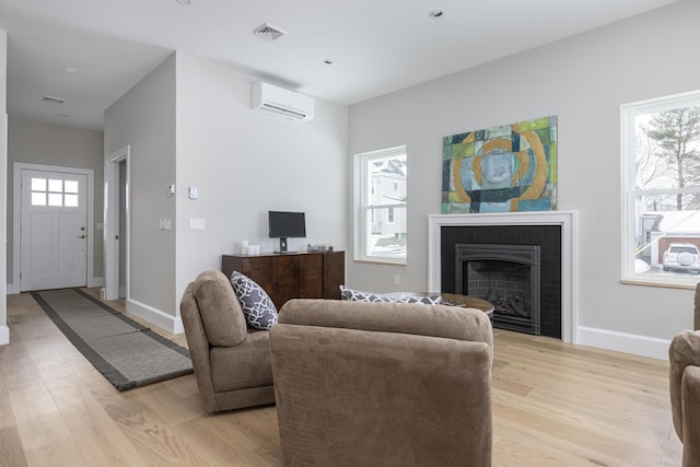 living room featuring a healthy amount of sunlight, a wall mounted air conditioner, and light wood-type flooring