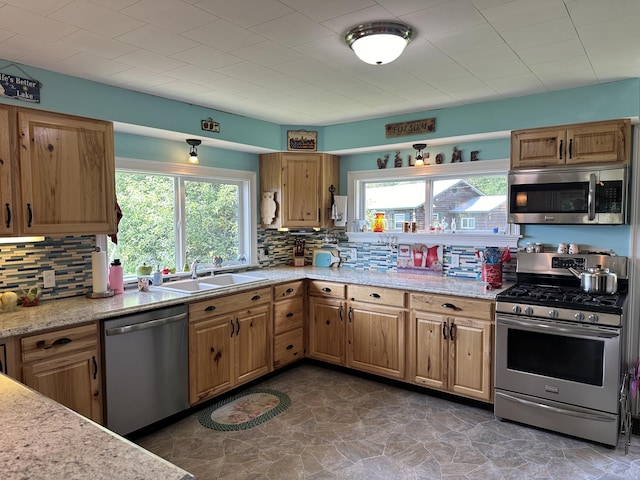 kitchen with sink, backsplash, stainless steel appliances, and light stone countertops