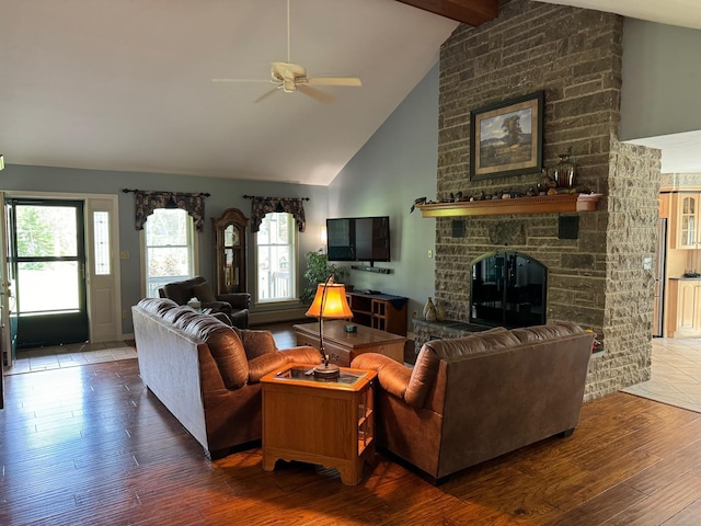 living room featuring wood-type flooring, ceiling fan, a stone fireplace, high vaulted ceiling, and beamed ceiling