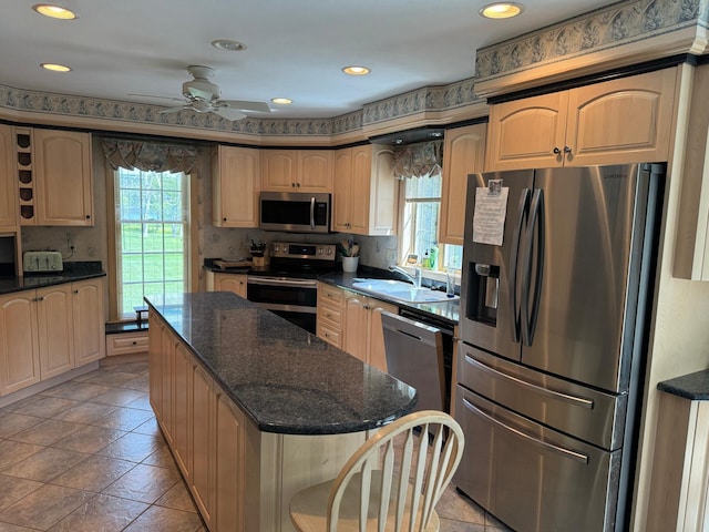 kitchen featuring ceiling fan, appliances with stainless steel finishes, sink, dark stone counters, and a kitchen island