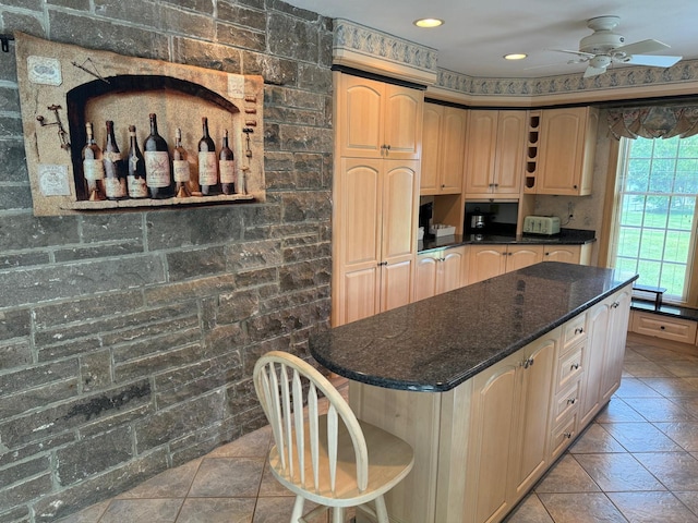 kitchen with a center island, light brown cabinets, tile patterned floors, dark stone counters, and ceiling fan