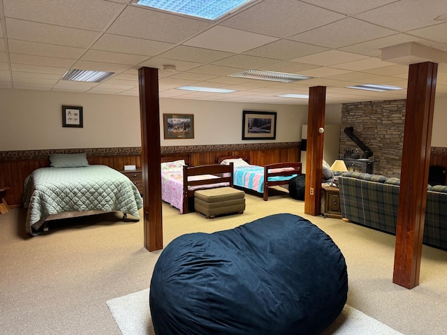 bedroom with a paneled ceiling, light colored carpet, and wooden walls