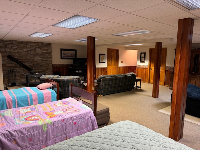 bedroom featuring a wood stove, carpet, a paneled ceiling, and wood walls