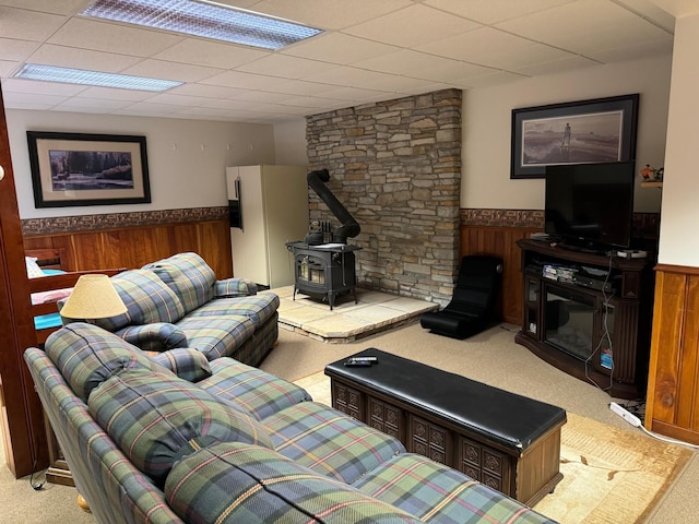 living room with a paneled ceiling, a wood stove, and wooden walls