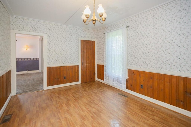 empty room with hardwood / wood-style flooring, crown molding, and an inviting chandelier