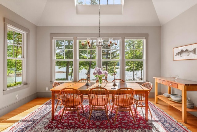 dining space featuring vaulted ceiling, a wealth of natural light, hardwood / wood-style flooring, and a notable chandelier