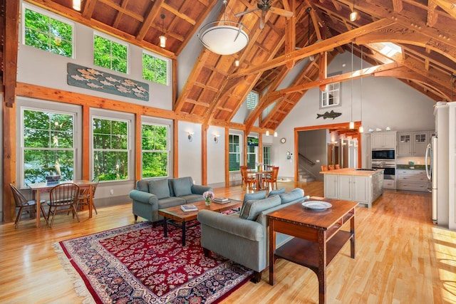 living room with high vaulted ceiling, light hardwood / wood-style flooring, beam ceiling, and ceiling fan