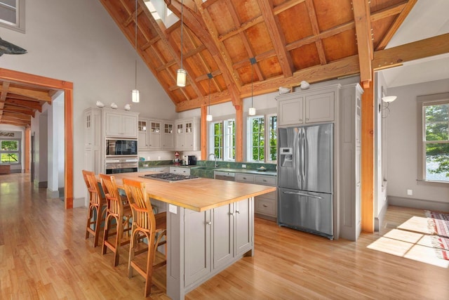 kitchen with a kitchen island, hanging light fixtures, stainless steel appliances, high vaulted ceiling, and butcher block counters