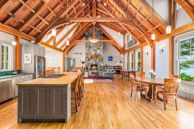 kitchen with decorative light fixtures, a center island, appliances with stainless steel finishes, a stone fireplace, and high vaulted ceiling