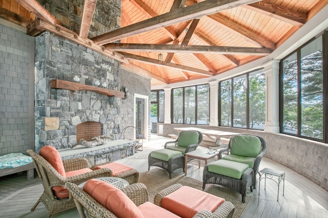 sunroom featuring a stone fireplace, plenty of natural light, lofted ceiling with beams, and wood ceiling