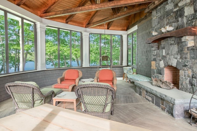 sunroom / solarium featuring vaulted ceiling with beams, wood ceiling, and a stone fireplace