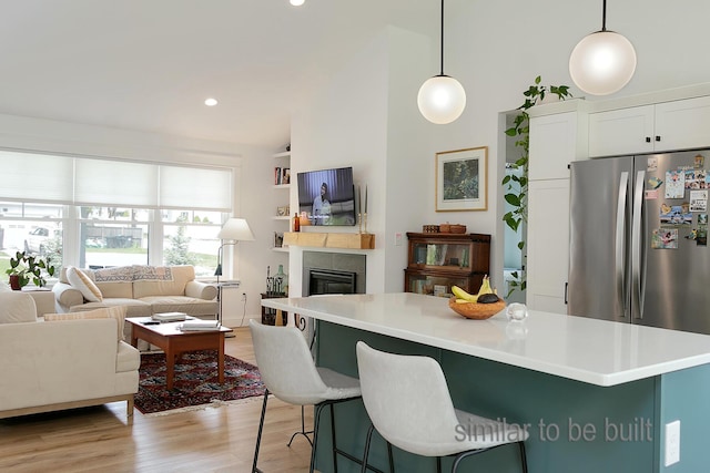 kitchen with lofted ceiling, a kitchen bar, white cabinetry, hanging light fixtures, and a tiled fireplace