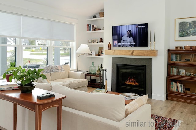 living room with light hardwood / wood-style floors, built in features, and a tile fireplace