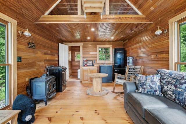 living room with wooden walls, wooden ceiling, light hardwood / wood-style floors, a wood stove, and lofted ceiling