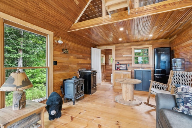 living room featuring vaulted ceiling, a wood stove, wooden walls, and light hardwood / wood-style flooring