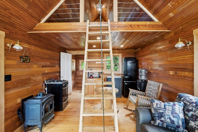 living room featuring lofted ceiling, wood walls, light wood-type flooring, and a wood stove