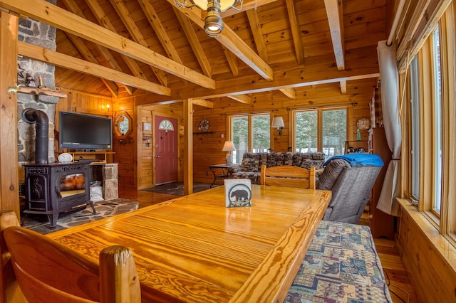 dining space featuring wood ceiling, lofted ceiling with beams, a wood stove, and wood walls