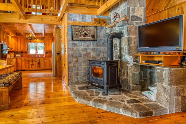 living room with wood walls, a wood stove, light hardwood / wood-style floors, wooden ceiling, and beam ceiling