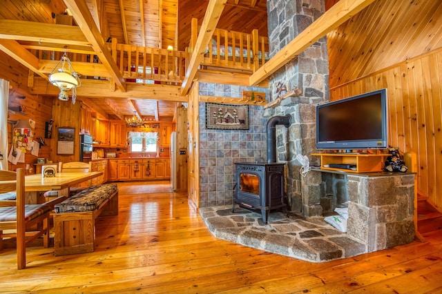 living room featuring wood walls, beamed ceiling, and a wood stove