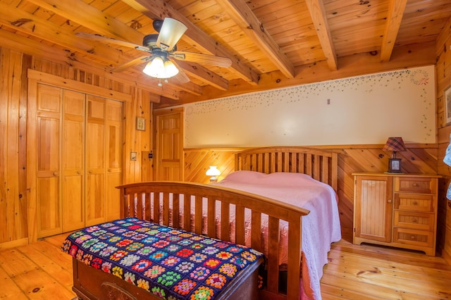 bedroom featuring wood walls, a closet, beamed ceiling, ceiling fan, and light hardwood / wood-style floors