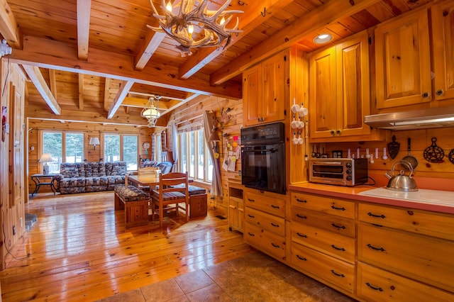 kitchen featuring black oven, wooden walls, a notable chandelier, light hardwood / wood-style floors, and beamed ceiling