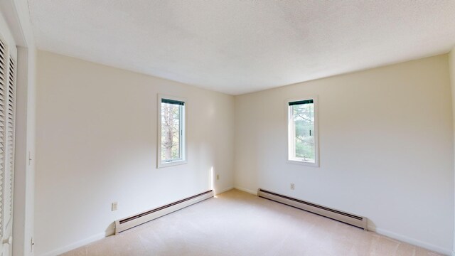 carpeted spare room with a textured ceiling and a baseboard heating unit