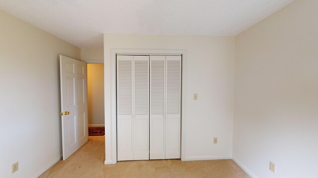 unfurnished bedroom with light colored carpet and a closet