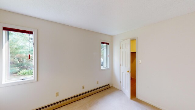 carpeted empty room featuring a wealth of natural light and a baseboard heating unit