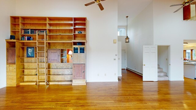 unfurnished living room featuring hardwood / wood-style flooring, a baseboard radiator, a towering ceiling, and ceiling fan