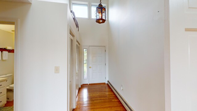 corridor featuring hardwood / wood-style floors, a towering ceiling, and baseboard heating