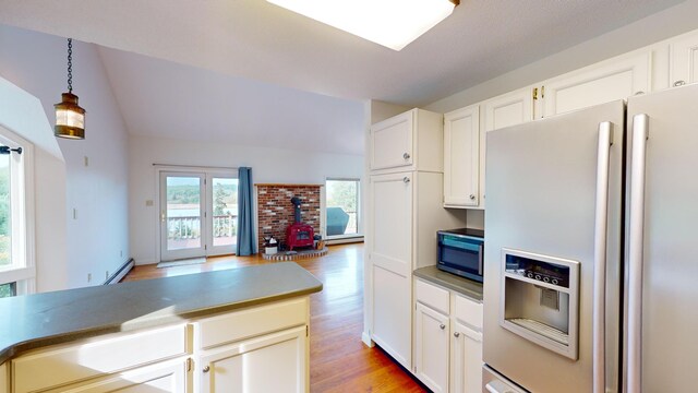 kitchen with a wood stove, white cabinetry, fridge with ice dispenser, decorative light fixtures, and light wood-type flooring