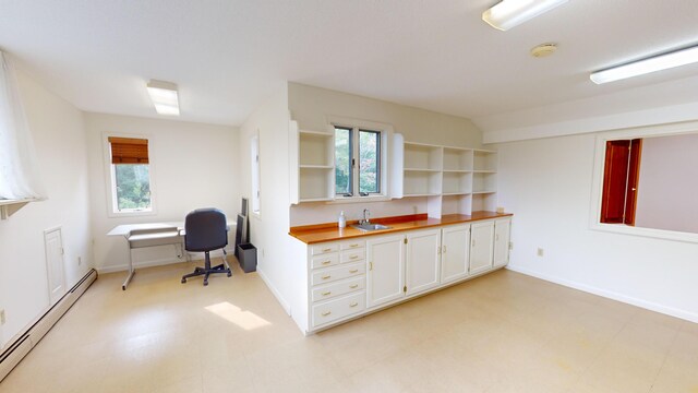 kitchen featuring white cabinetry, plenty of natural light, butcher block counters, and baseboard heating