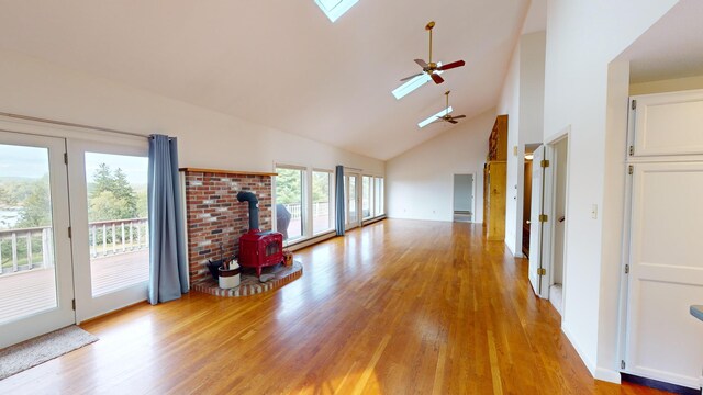 unfurnished living room featuring ceiling fan, a skylight, high vaulted ceiling, light hardwood / wood-style floors, and a wood stove